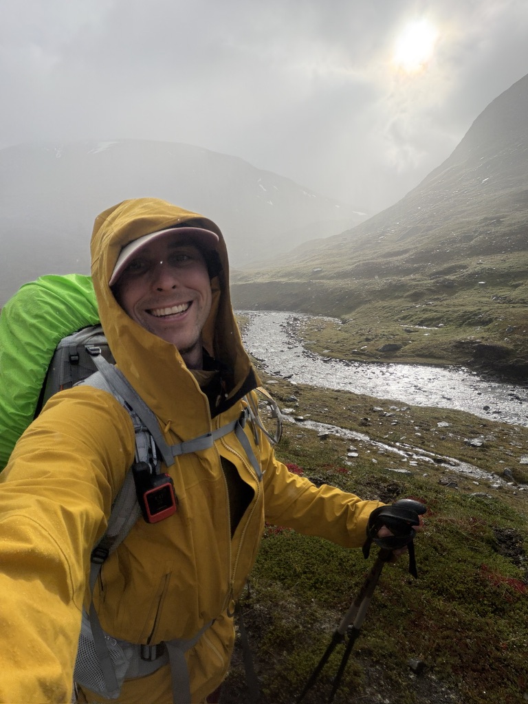 Hiker in a yellow rain jacket crossing a misty Lapland valley