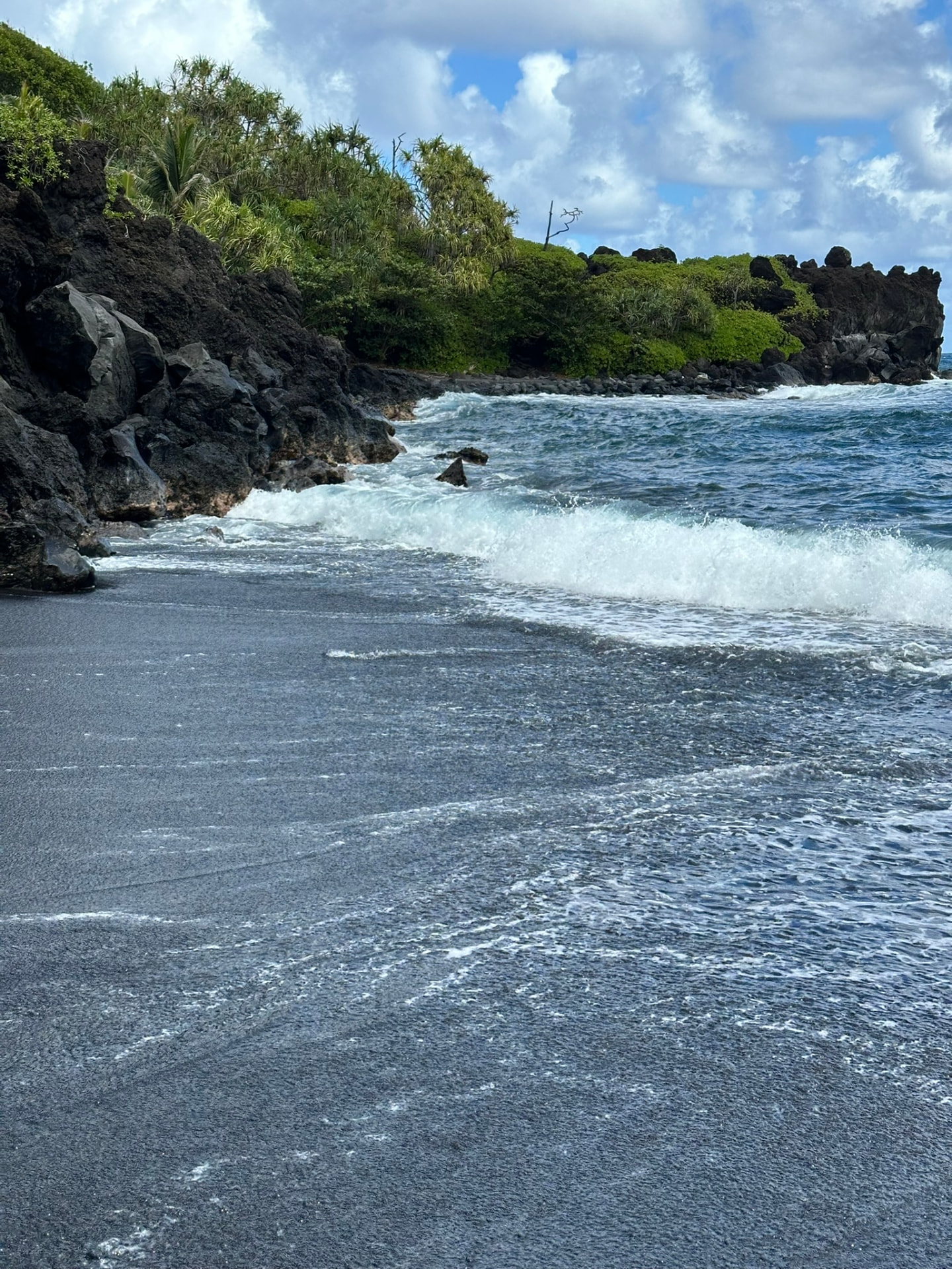Black lava sand beach with white surf rolling in and green jungle behind