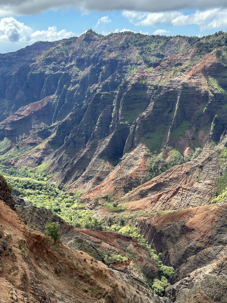 Red and green eroded canyon walls under a partly cloudy sky