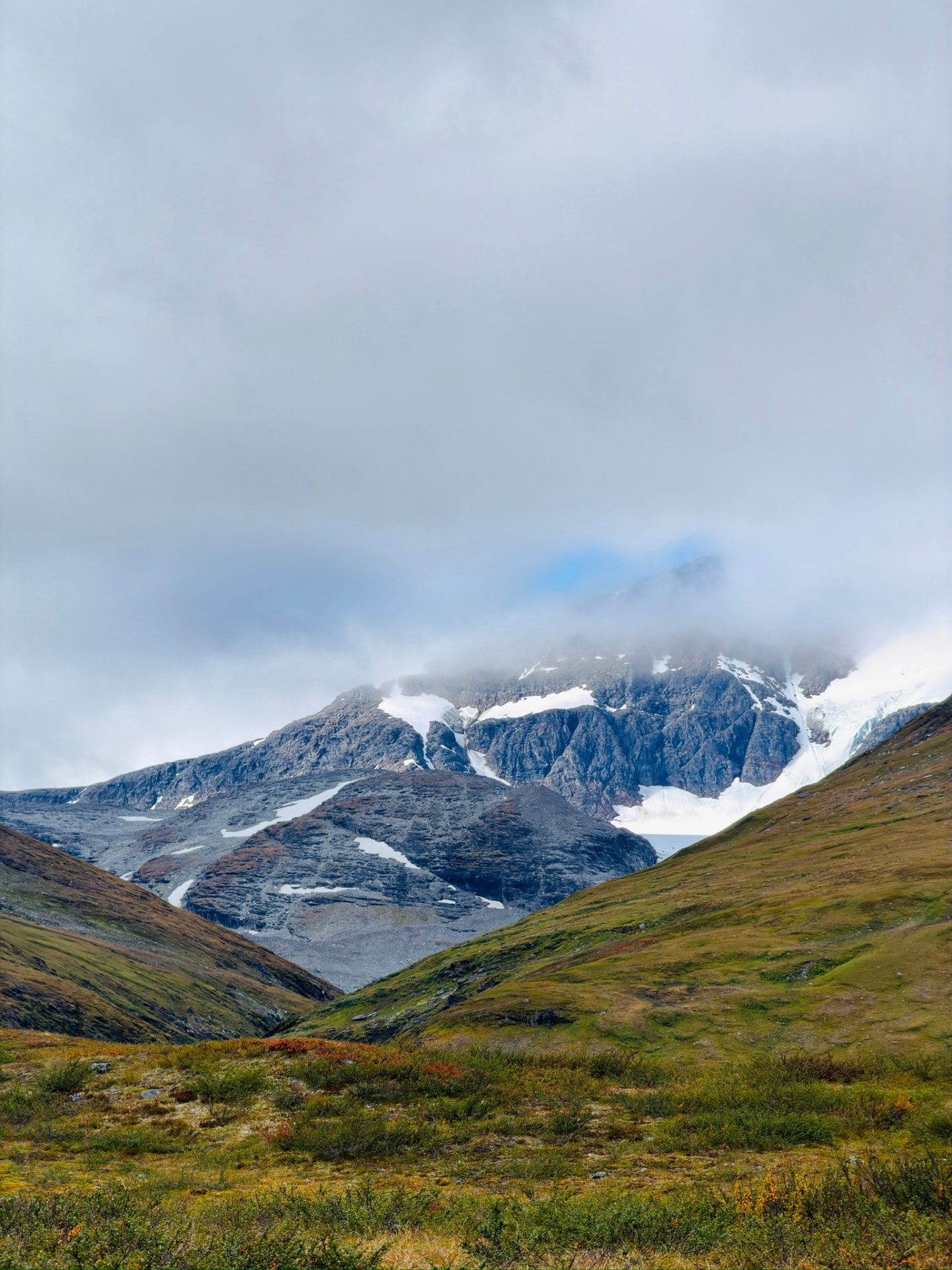 Glaciated mountain emerging through cloud above a green valley