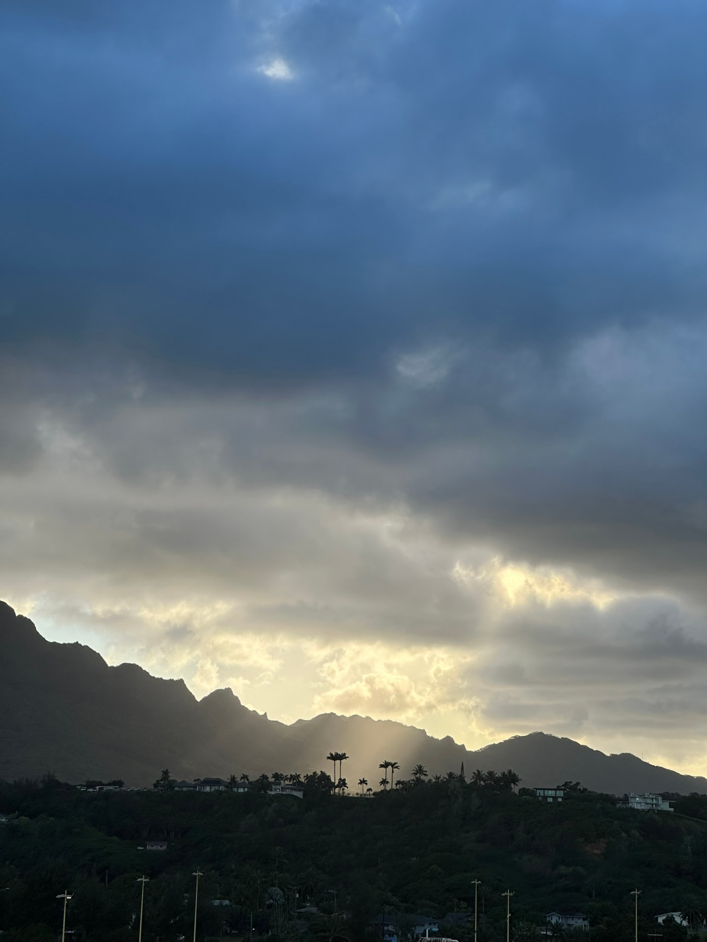 Sunlight breaking through dark storm clouds over jagged peaks at dusk