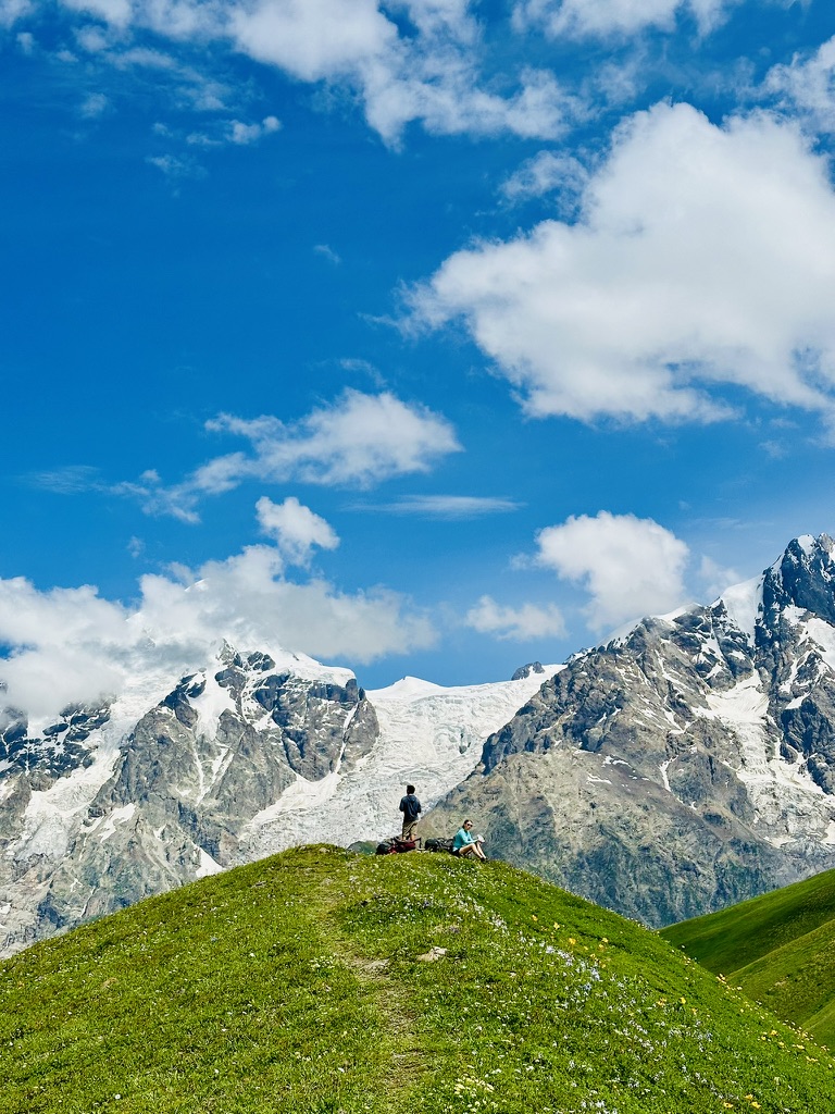 Two hikers resting on a flower meadow below a glacier