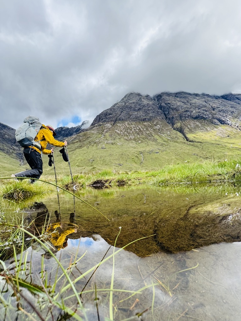 Backpacker reflected in a still pool below a misty ridge