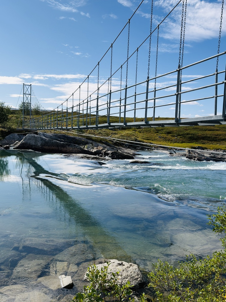 Suspension bridge crossing a clear blue mountain river