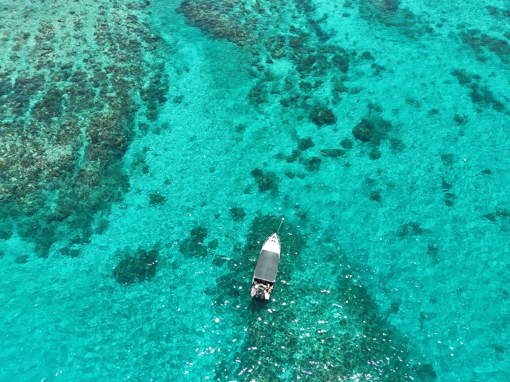 Aerial view of a small boat floating over a turquoise reef flat