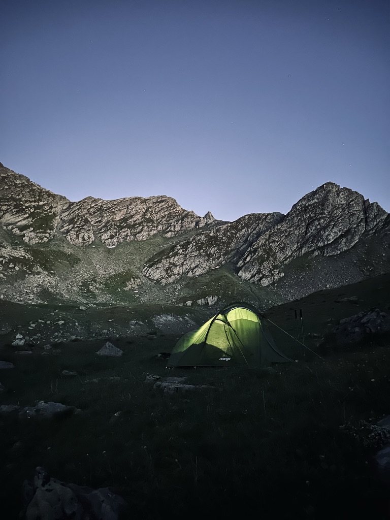 Glowing tent pitched below rocky summits at dusk