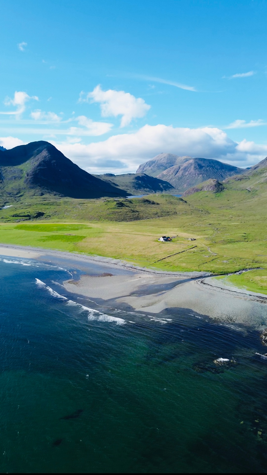 Aerial view of a white sandy beach and a lone croft beneath the hills