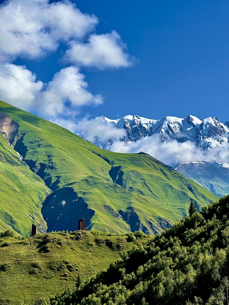 Stone tower ruins on a green ridge with snowy peaks behind