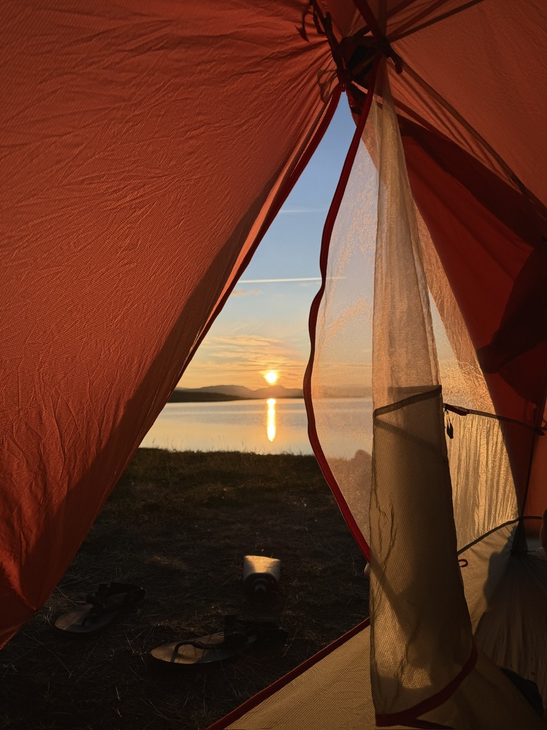Sunset over a lake viewed from inside a red hiking tent