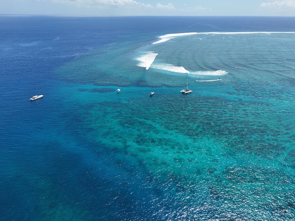 Aerial view of a breaking reef pass with boats anchored in the lagoon