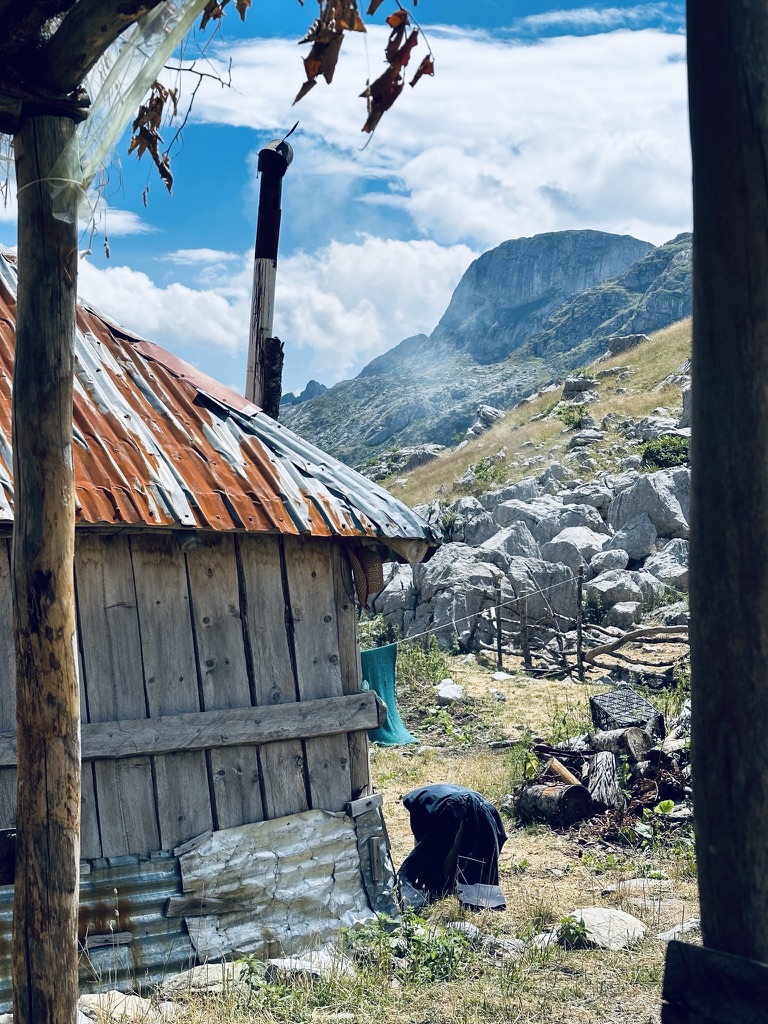 Rust-roofed shepherds hut with a wood stove chimney smoking in the mountains