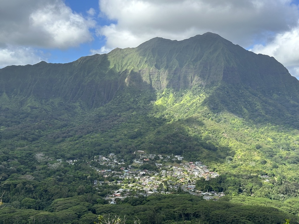Steep green ridgelines above a small town tucked into a lush Hawaiian valley